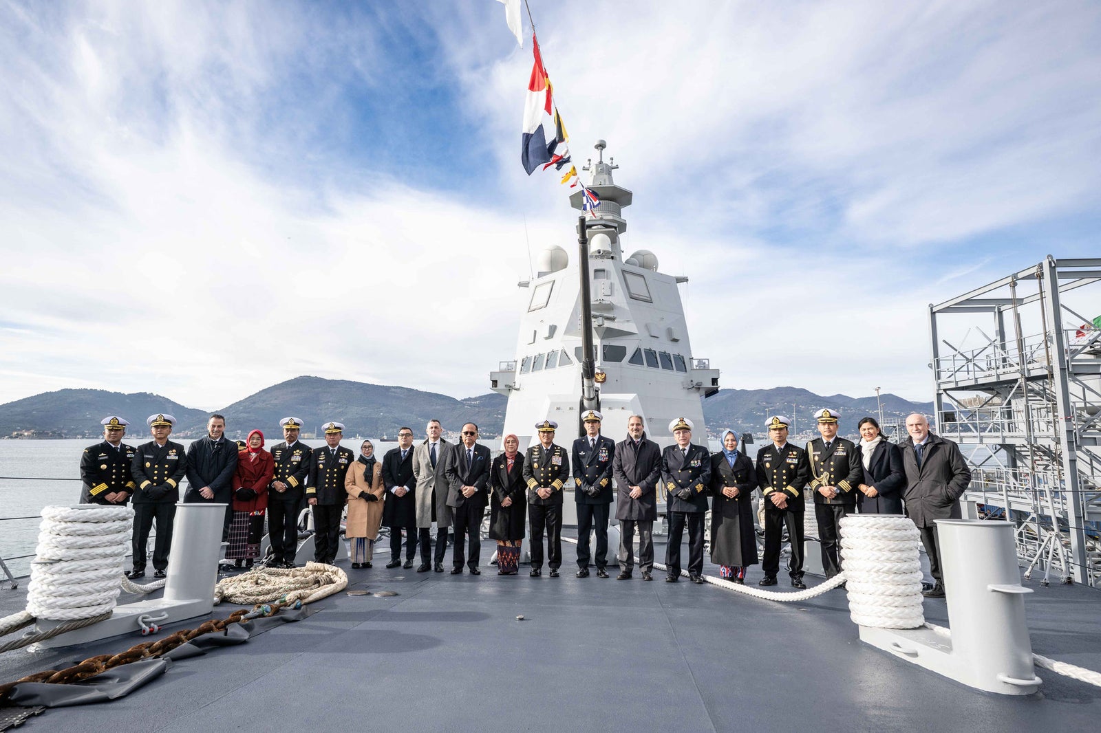 newsroom - press releases - 2025 - fincantieri group: fincantieri delivers the ppa "kri prabu siliwangi-321" to the indonesian navy: group of officers and representatives posing on the deck of the ppa "kri prabu siliwangi-321", mooring ropes in the foreground, ship’s superstructure and flags in the background, mountains and sea.