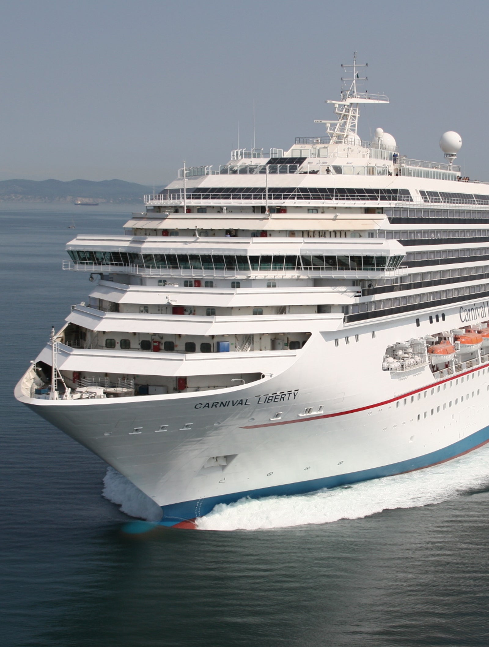Fincantieri | Gruppo - Business - Prodotti - Navi da Crociera - Carnival Liberty: Vista laterale della nave Carnival Liberty operativa in navigazione, scafo bianco con fumaiolo rosso, ponti passeggeri multipli e scialuppe visibili.