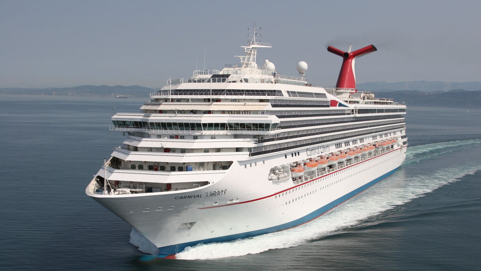  Fincantieri | Gruppo - Business - Prodotti - Navi da Crociera - Carnival Liberty: Vista laterale della nave Carnival Liberty operativa in navigazione, scafo bianco con fumaiolo rosso, ponti passeggeri multipli e scialuppe visibili.
