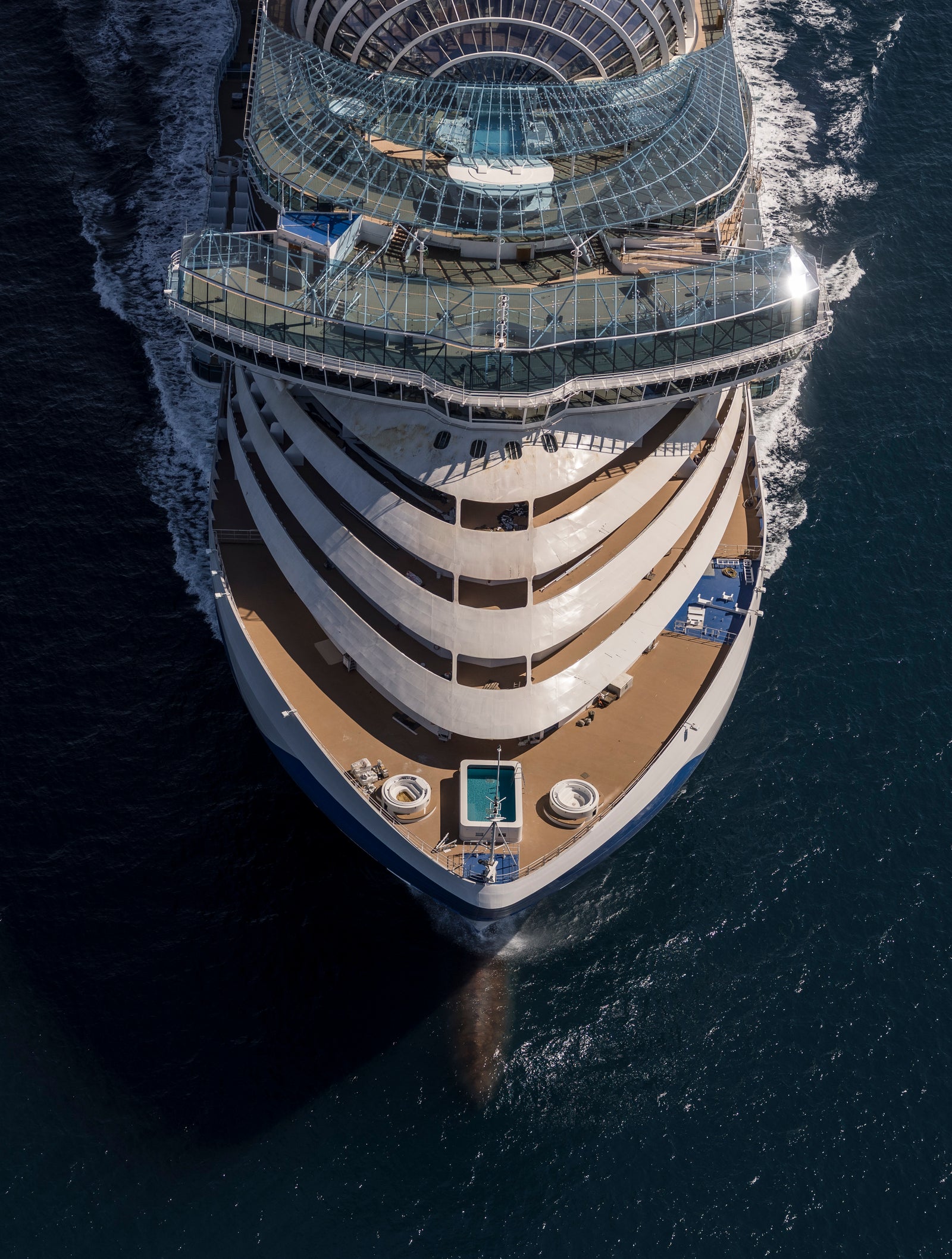 Fincantieri | Gruppo - Business - Prodotti - Navi da Crociera - Star Princess: Aerial view of large luxury cruise ship in operation, navigating calm deep blue ocean, multiple decks with pool area and glass-enclosed structures, clear sky, expansive sea.