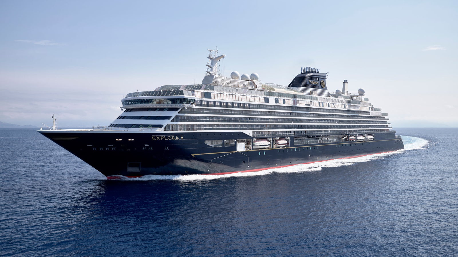 Fincantieri | Group - Business - Products - Cruise Ships - EXPLORA II: Side view of operational cruise ship in navigation, sleek black and white design, multiple decks and visible amenities, name Explora X clearly visible on hull.