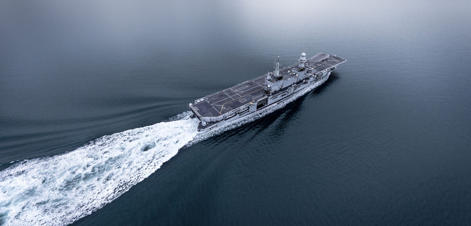 Fincantieri | Group - Business - Products - Naval Vessels - Aircraft Carriers and Amphibious Ships - Cavour: Top-down perspective of aircraft carrier "Cavour" underway, gray hull, expansive flight deck, distinct command tower, navigating open sea.