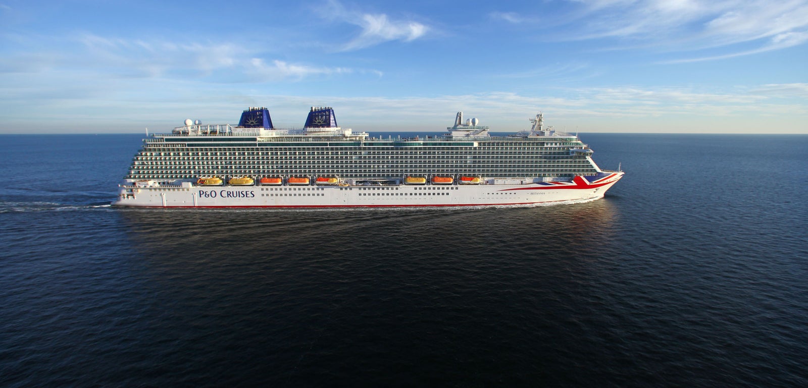 Fincantieri | Group - Business - Products - Cruise Ships - Britannia: Side view of Britannia P&O Cruises ship in operation navigating open sea, hull with red and white Union Jack design on bow, two blue funnels, visible lifeboats, P&O Cruises text on side.
