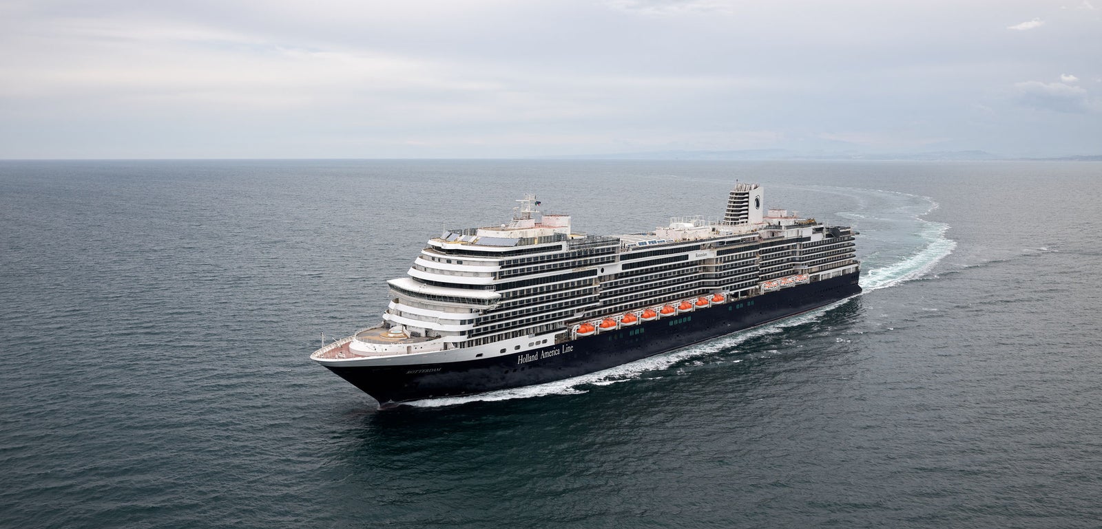 Fincantieri | Group - Business - Products - Cruise Ships - Rotterdam: Modern operational cruise ship navigating calm open waters under cloudy sky, multiple decks and elegant design, ideal for leisure travel.