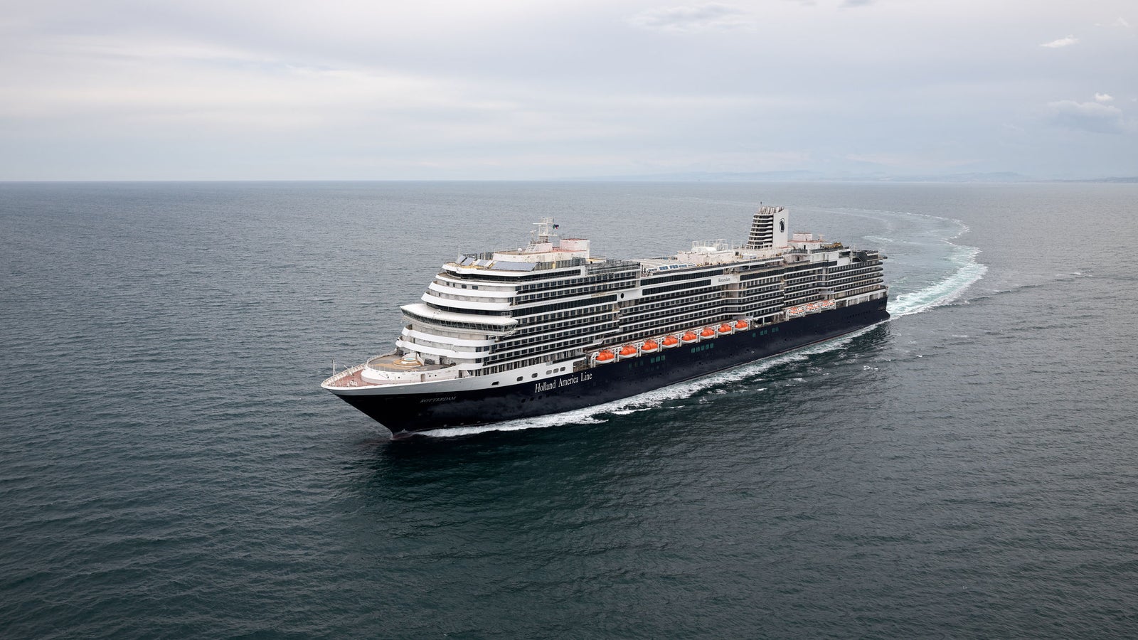 Fincantieri | Group - Business - Products - Cruise Ships - Rotterdam: Modern operational cruise ship navigating calm open waters under cloudy sky, multiple decks and elegant design, ideal for leisure travel.