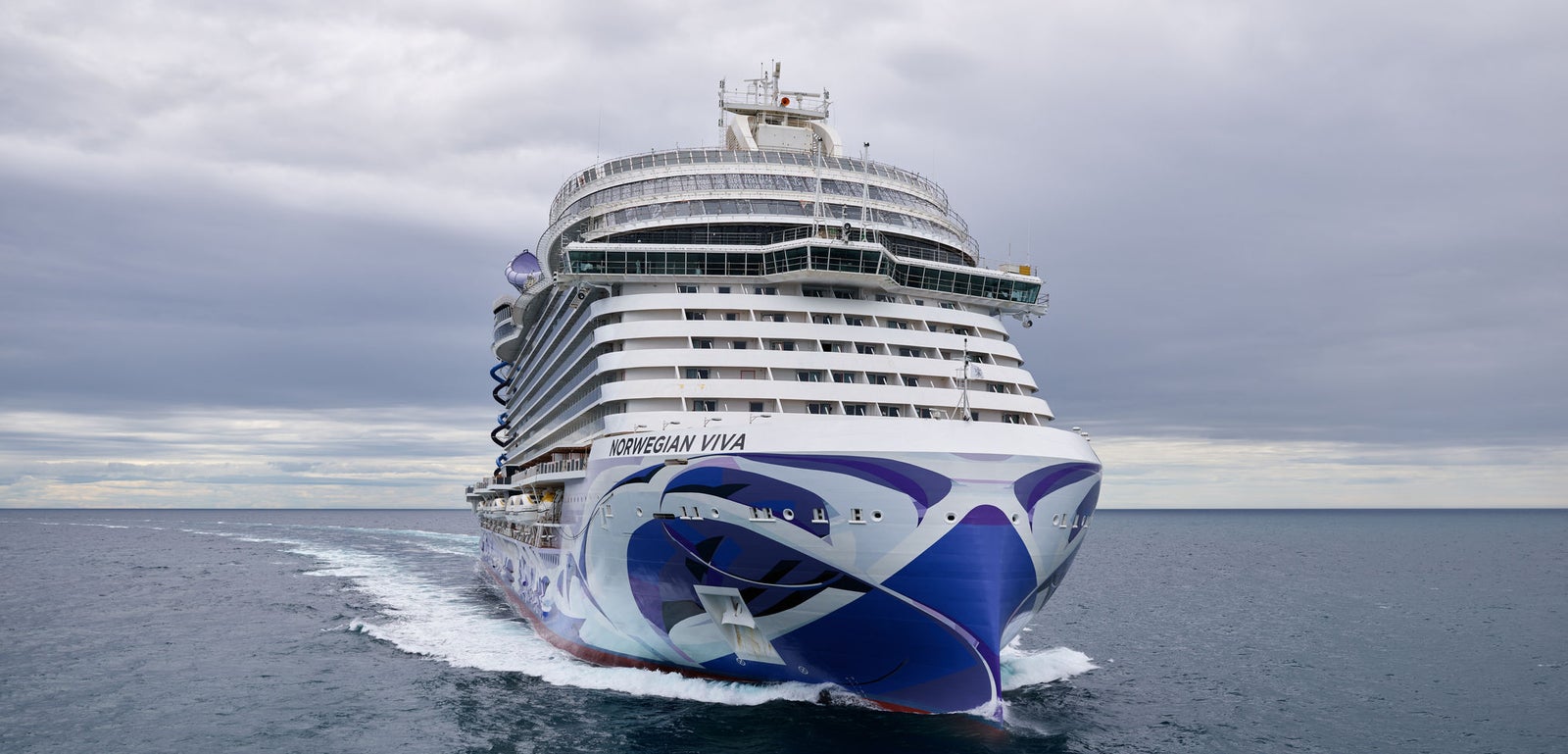 Fincantieri | Gruppo - Business - Prodotti - Navi da Crociera - Norwegian Viva: Nave da crociera Norwegian Viva operativa in navigazione su acque calme sotto cielo nuvoloso, scafo con audace design blu e bianco, nome 'Norwegian Viva' visibile.