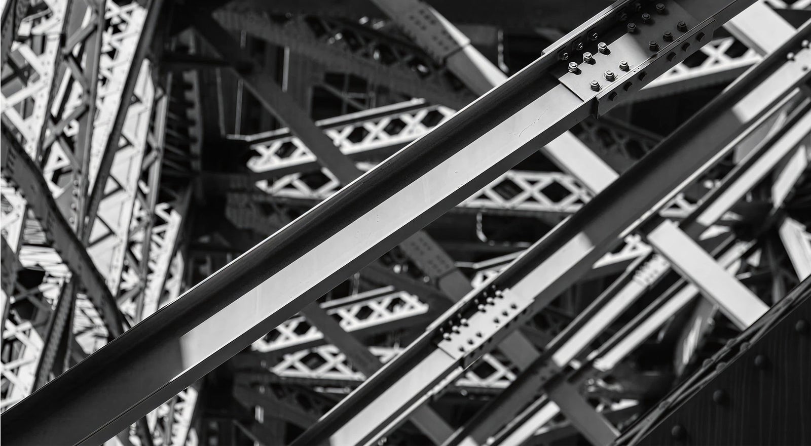 Fincantieri | Group - Subsidiaries and Affiliates - Fincantieri Infrastructure: Close-up view of intersecting steel beams with intricate structural details; monochrome palette emphasizes industrial design and geometric patterns, rivets and metal textures highlighted for bold architectural visual impact.
