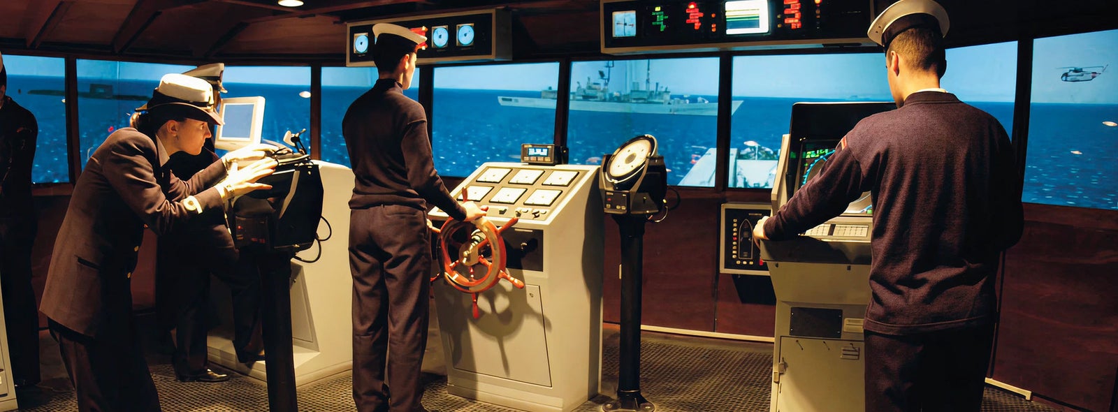 Fincantieri | Business Services - After-Sales Services - Training & Support: A group of naval officers operates a maritime simulation system in a control room setting. The environment features multiple screens displaying ocean visuals and ship controls, including steering wheels and monitoring equipment. The officers are dressed in formal uniforms, and the scene conveys a professional and focused atmosphere.
