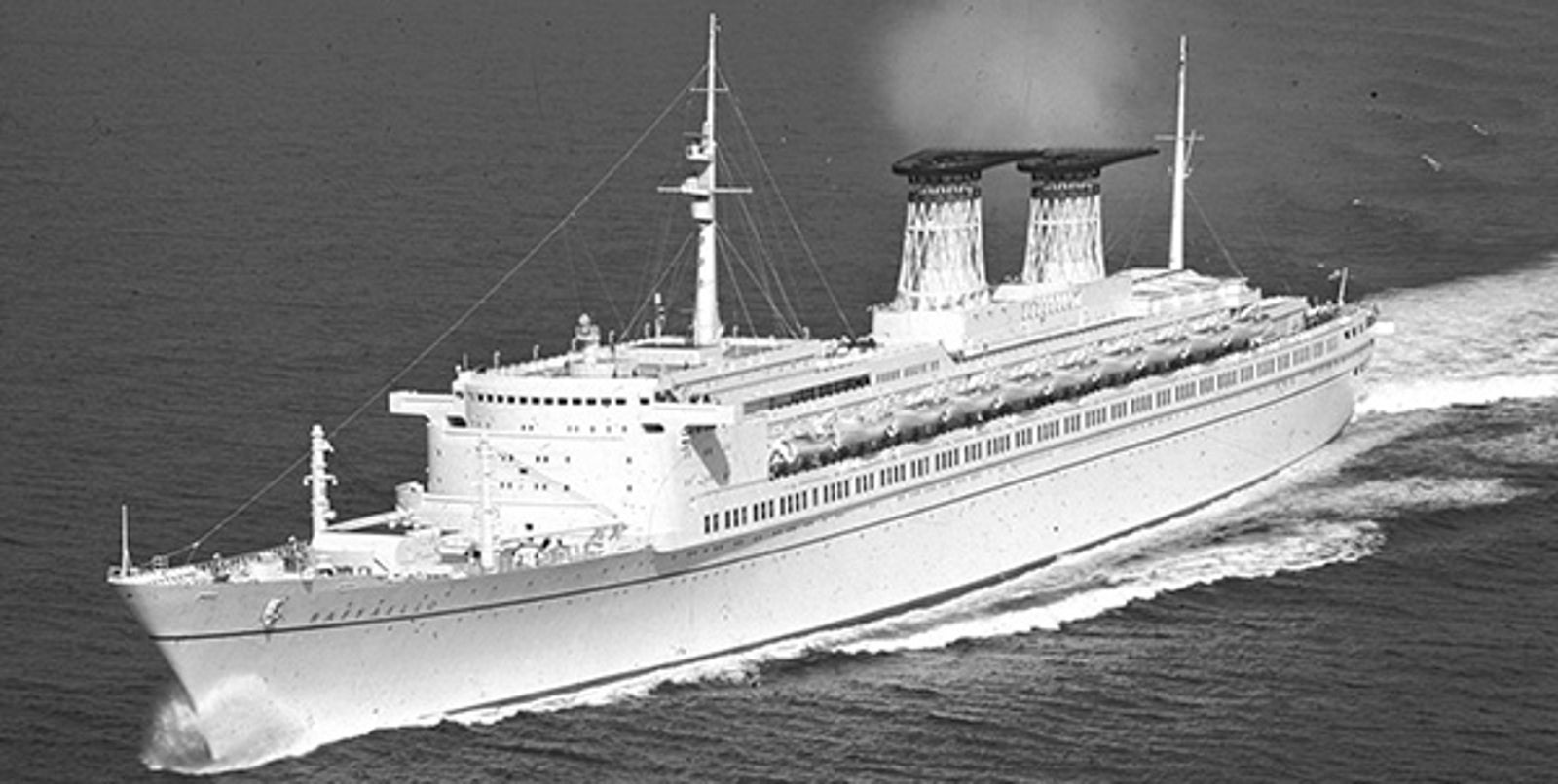 Fincantieri | About Us - Historic Ships: Large ocean liner sailing on calm waters, light smoke from the two funnels, sleek and streamlined ship design, black and white photo highlighting classic maritime architecture.