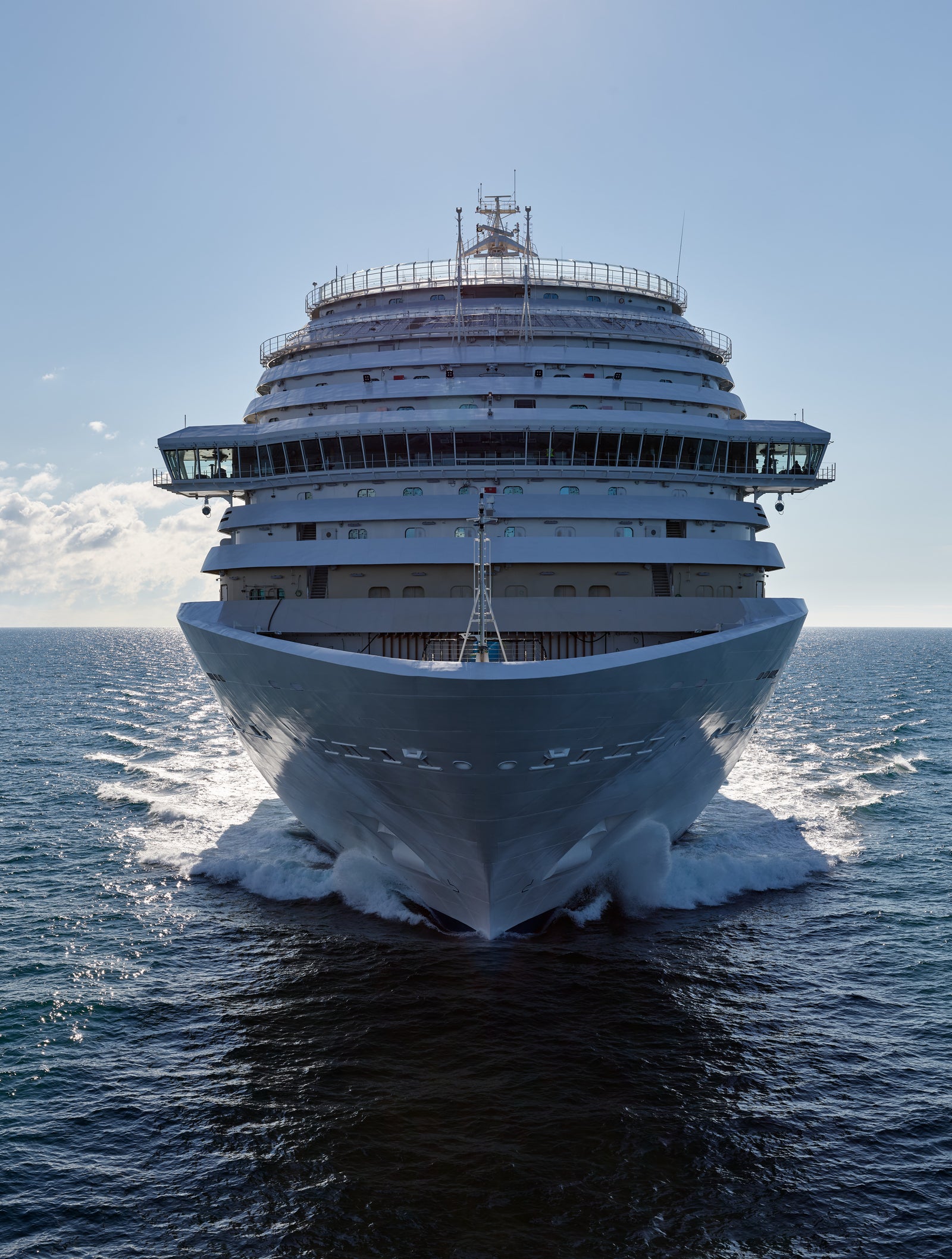 Fincantieri | Group - Business - Products - Cruise Ships - Costa Firenze: Front view of large operational Costa Firenze cruise ship with multi-deck structure and elegant design, sailing on calm waters with clear sky and sunlight reflections, serene and majestic scene.
