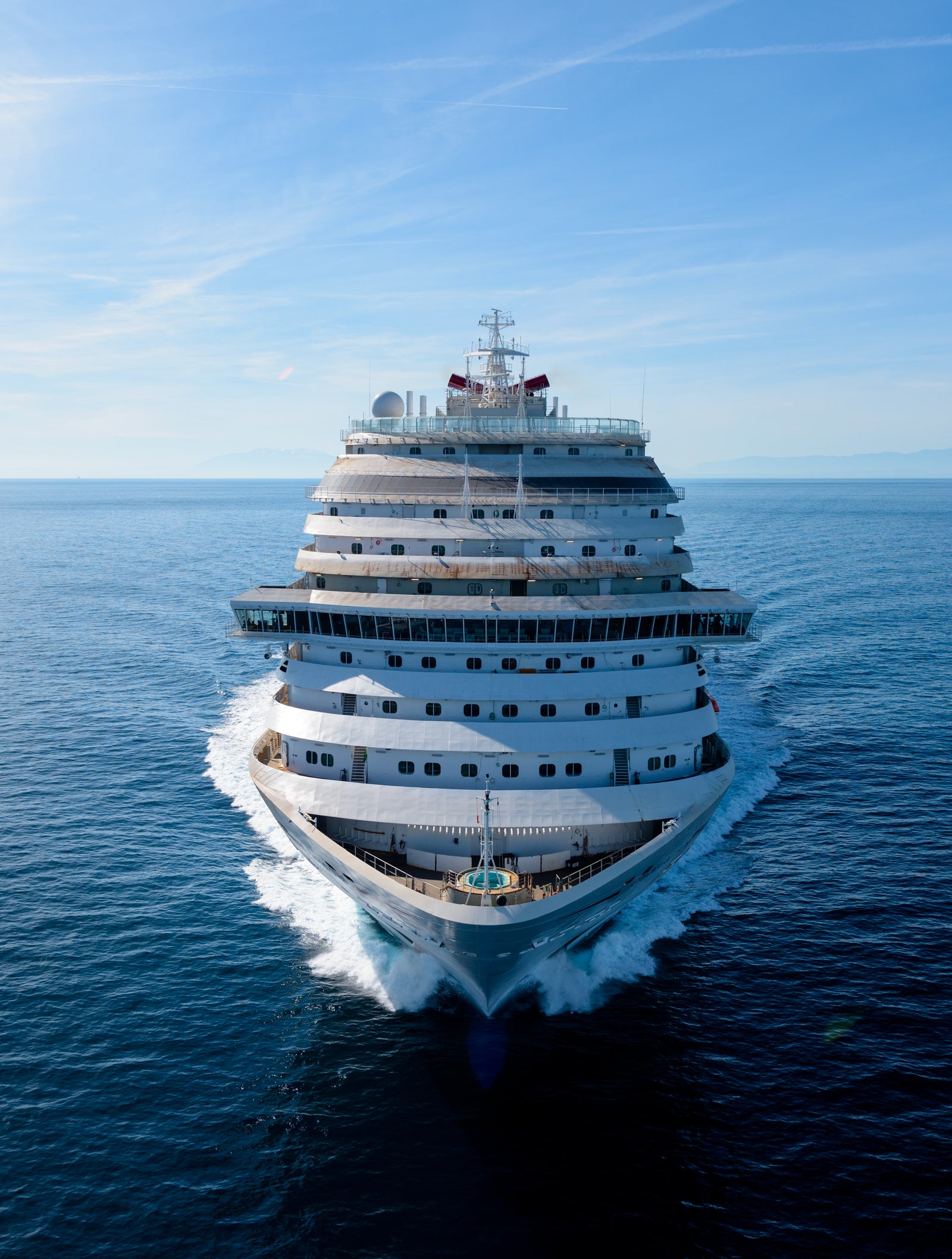 Fincantieri | Group - Business - Products - Cruise Ships - Carnival Horizon: Front view of large operational white cruise ship navigating calm open waters under serene blue sky, structure with multiple decks and sleek design, highlights grandeur and modernity, tranquil ocean context emphasizes peaceful journey.