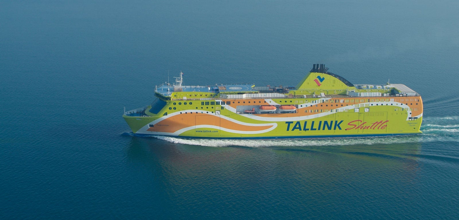 Fincantieri | Group - Business - Products - Ferries - Superstar: Brightly colored Tallink Shuttle ferry in operation, green and orange design, visible branding and text, modern structure, sailing across calm blue waters, open sea.