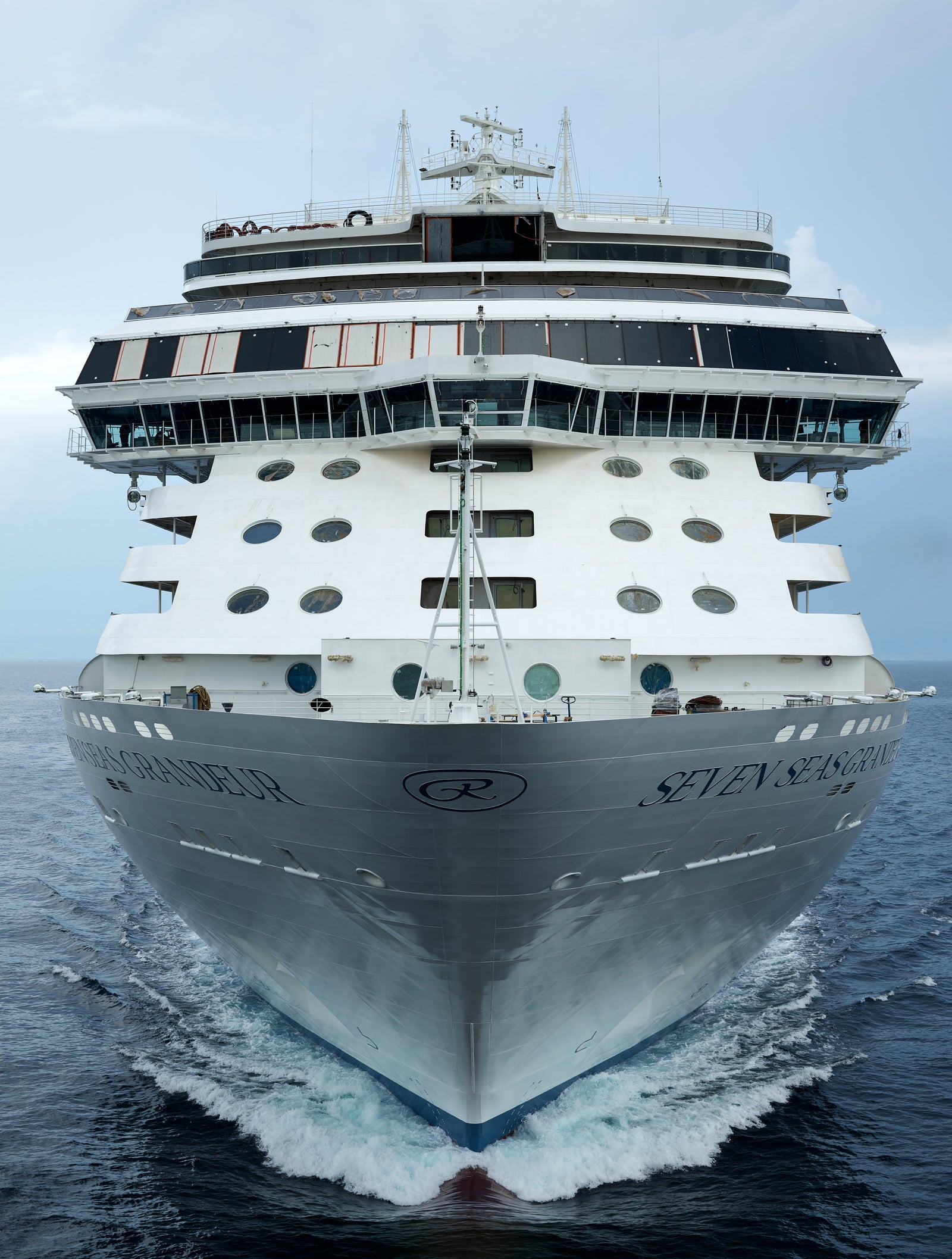 Fincantieri | Group - Business - Products - Cruise Ships - Seven Seas Grandeur: Large modern operational cruise ship with multiple decks and visible lifeboats, front view, sailing on calm waters under clear sky, deck spaciousness and elegance, visible wake.