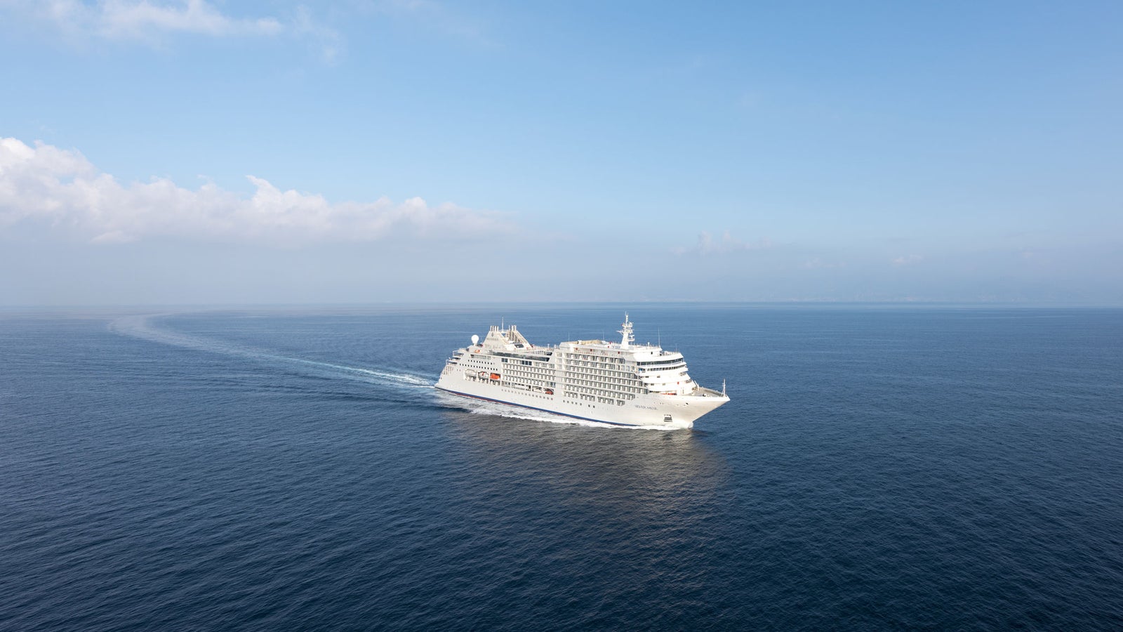 Fincantieri | Group - Business - Products - Cruise Ships - Silver Muse: Large luxury cruise ship in operation with white exterior and multiple decks, balconies and relaxation spaces, sailing on calm waters under partly cloudy sky, visible wake, atmosphere of elegance and relaxing travel.