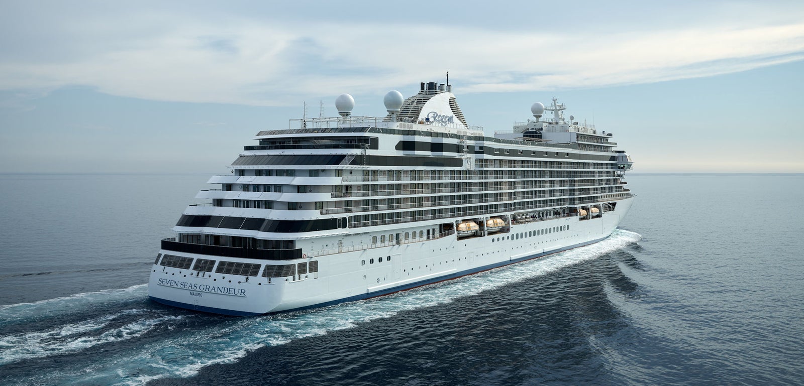 Fincantieri | Group - Business - Products - Cruise Ships - Seven Seas Splendor: Large operational luxury cruise ship with multiple decks and visible lifeboats, sailing on calm waters under partly cloudy sky, bow clearly visible, 'Seven Seas Splendor' name on hull, wide views of the open ocean.