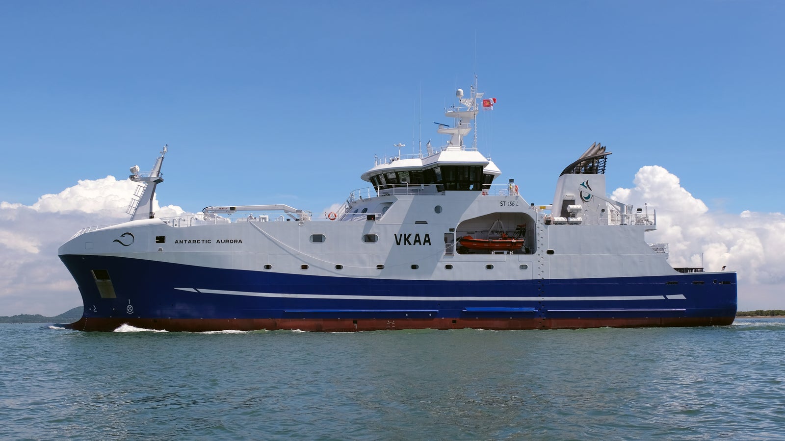 Prodotto - Peschereccio Antarctic Aurora: Vista laterale della nave operativa su acque calme, scafo bianco e blu con nomi Antarctic Aurora e Hobart ben visibili, design moderno, equipaggiamenti di coperta presenti, cielo sereno.