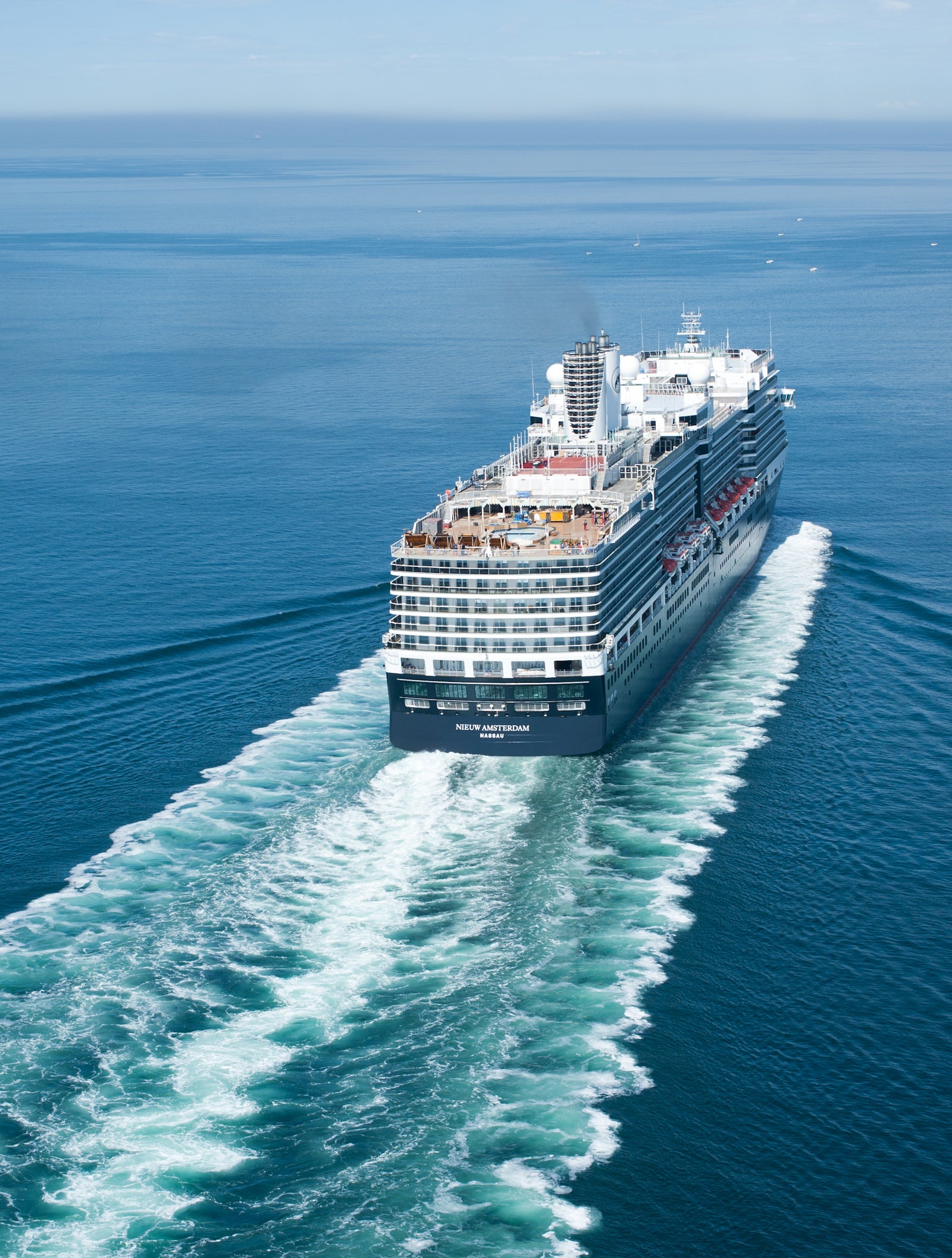Fincantieri | Group - Business - Products - Cruise Ships - Nieuw Amsterdam: Large luxury cruise ship in operation sailing on calm open waters under clear blue sky, multiple decks including outdoor pool area and relaxation spaces, ship’s wake creates dynamic visual contrast with serene sea.