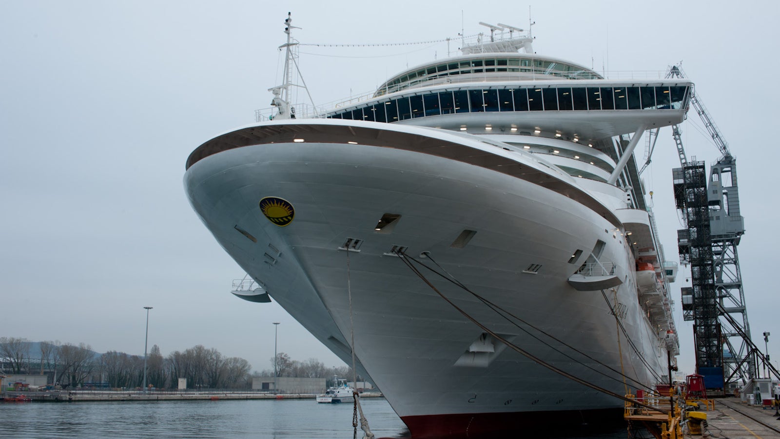 Fincantieri | Group - Business - Products - Cruise Ships - Azura: View of Azura cruise ship docked in port, white hull with multiple passenger decks, bow with visible circular emblem.