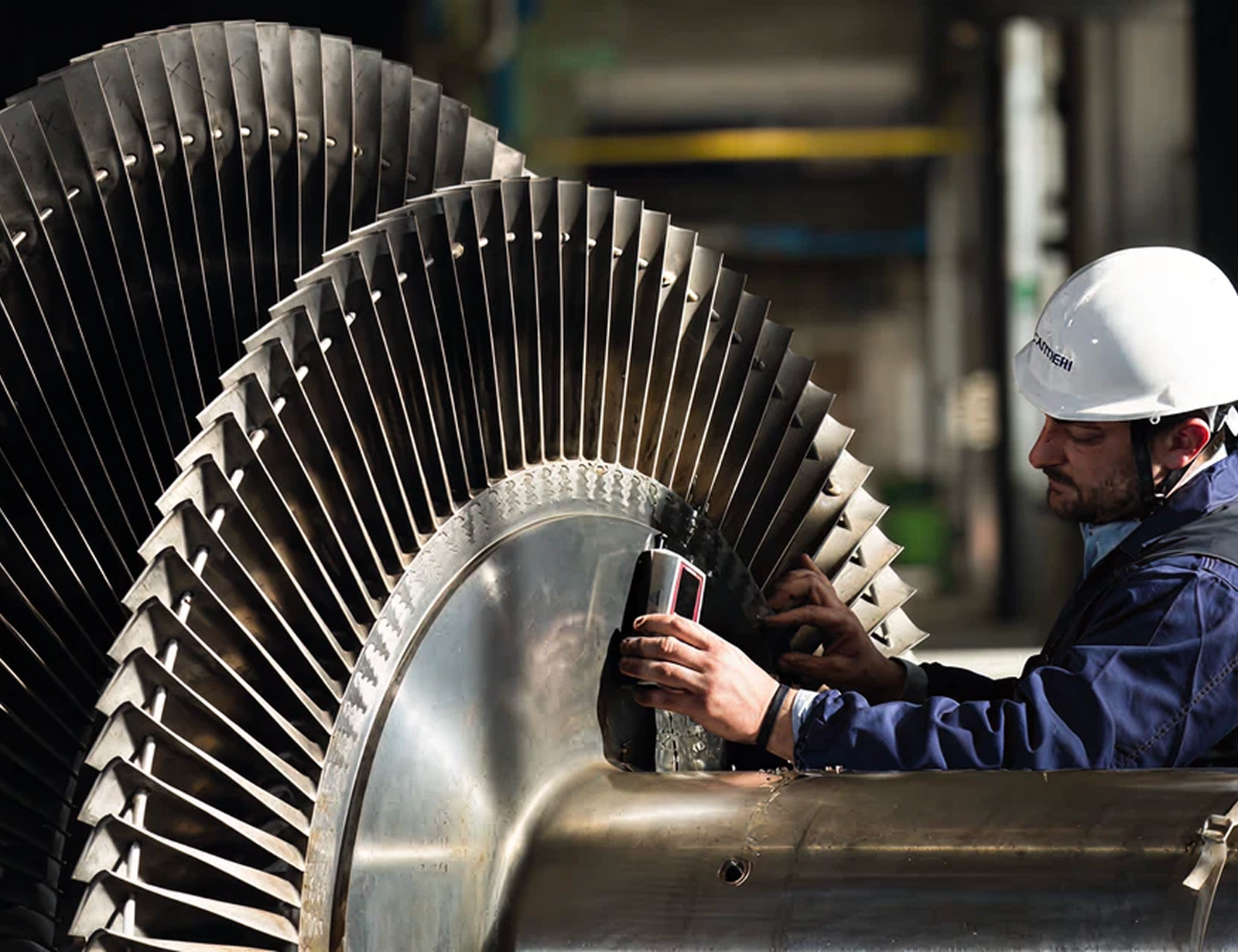 Fincantieri | Group - Business - Products - Equipment, Systems and Infrastructures - Steam turbines: Worker in hard hat inspecting blades of large industrial turbine, close-up highlights intricate turbine details and precise examination.