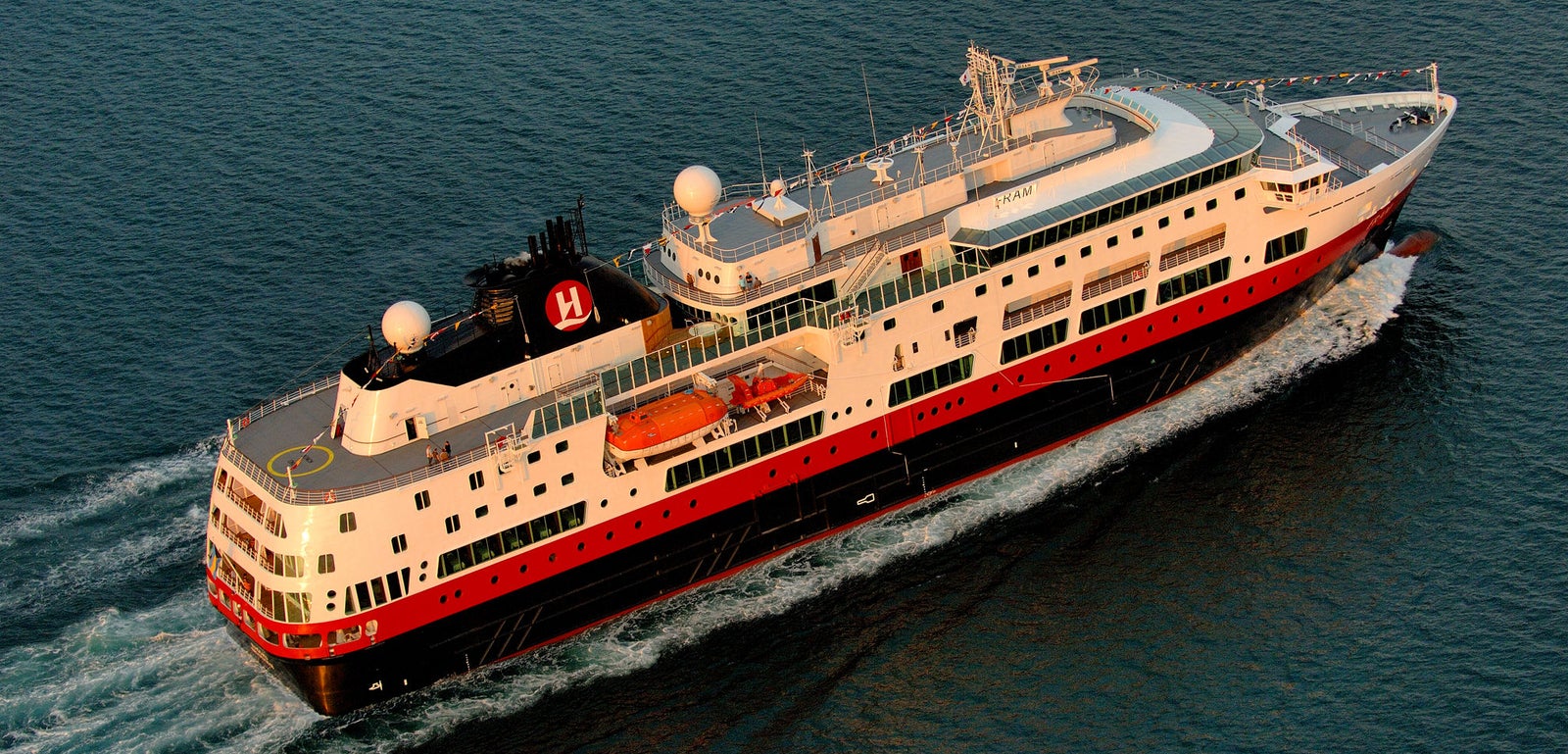 Fincantieri | Group - Business - Products - Cruise Ships - Fram: Large operational ship with red and black hull, multiple decks, helipad and visible lifeboats, 'H' logo clearly present on funnel, sailing on calm waters under partly cloudy sky, highlighting imposing structure and safety features.