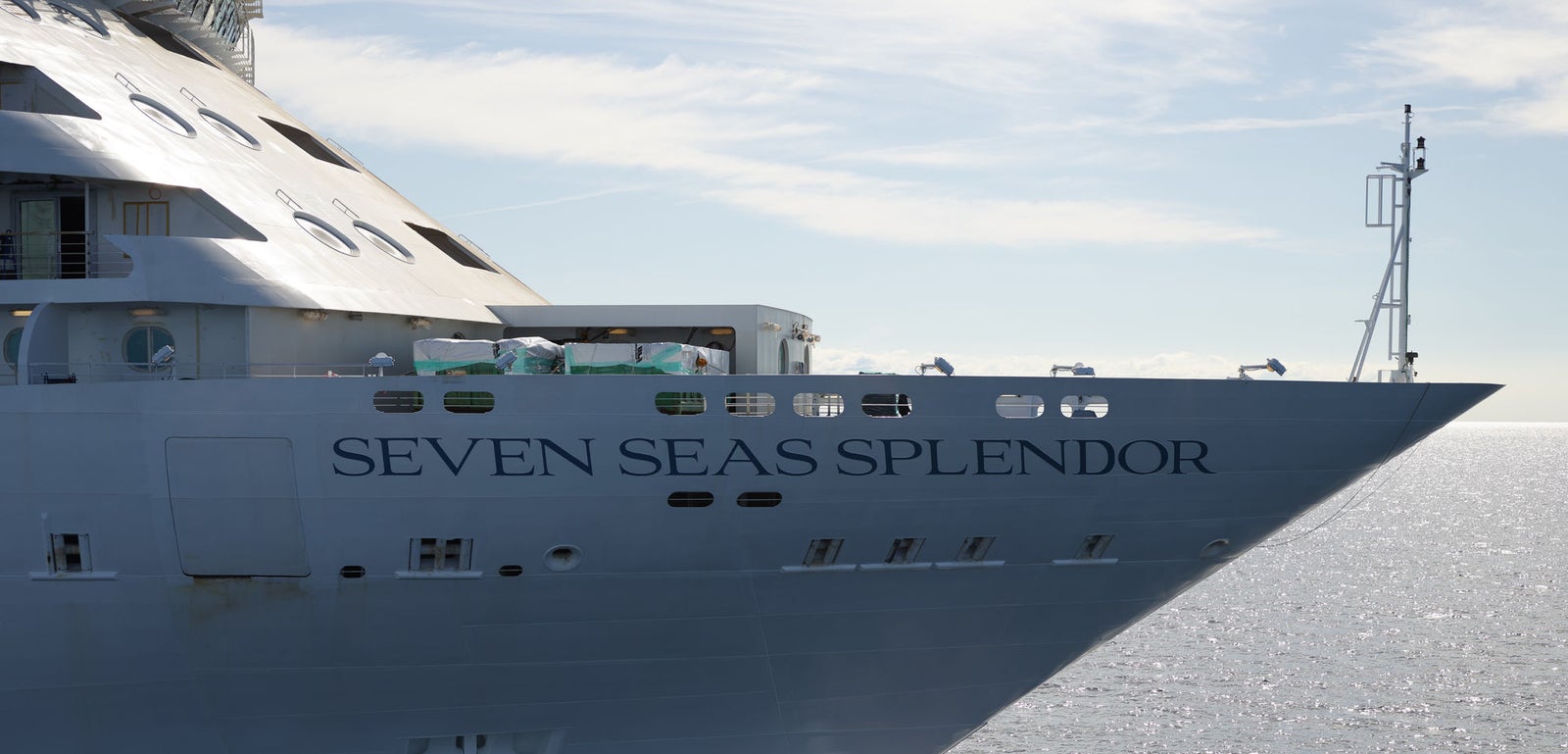 Fincantieri | Group - Business - Products - Cruise Ships - Seven Seas Splendor: Large operational luxury cruise ship with multiple decks, bow cutting through calm waters under clear blue sky, sunlight reflecting on ocean waves and distant horizon, serene scene highlighting sea vastness and refined travel experience.