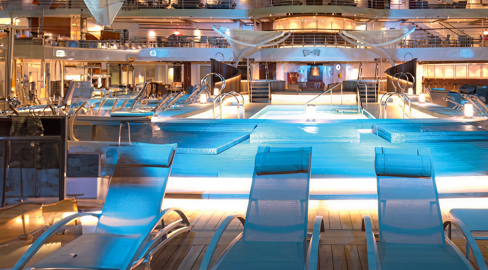  Fincantieri | Gruppo - Società - Controllate e collegate - Marine Interiors: Ponte piscina illuminato su nave da crociera di lusso, poltrone prendisole e piscine luminose, ambiente sereno e accogliente con illuminazione calda e design moderno; immagine che cattura eleganza e relax notturno a bordo.