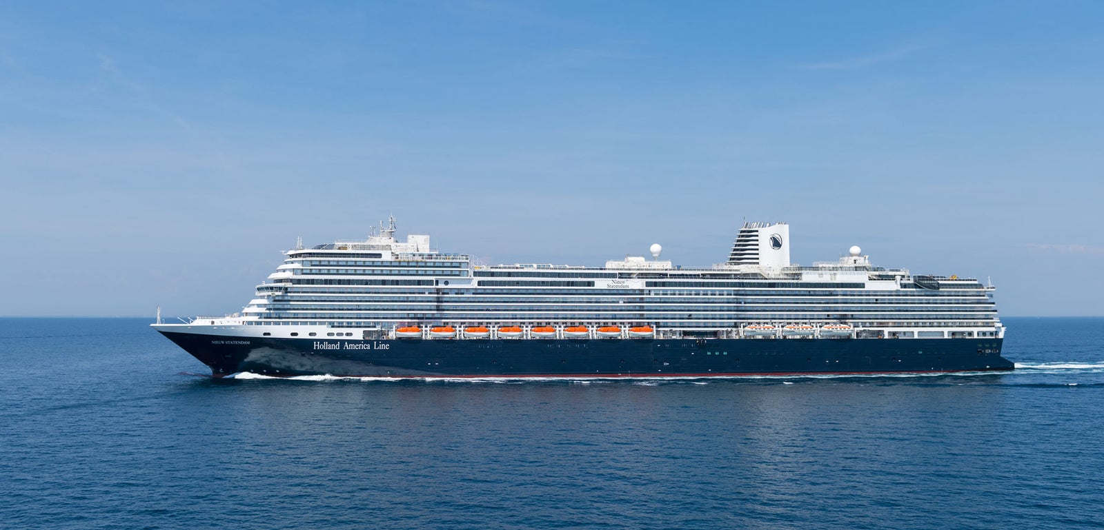  Fincantieri | Gruppo - Business - Prodotti - Navi da Crociera - Nieuw Statendam: Nave da crociera moderna operativa che scivola su acque calme e aperte sotto cielo azzurro limpido, più ponti e scialuppe di salvataggio visibili lungo i lati, nome Holland America Line chiaramente visibile sulla struttura esterna.
