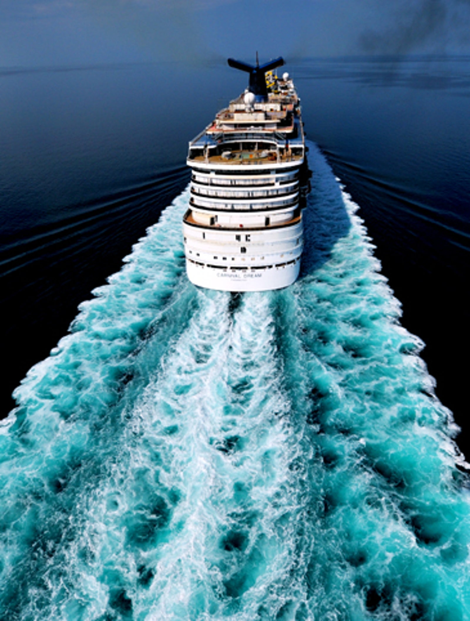Fincantieri | Group - Business - Products - Cruise Ships - Carnival Dream: Aerial view of large operational white cruise ship navigating calm sea, vivid turquoise wake, clear sky and vast ocean create tranquil and adventurous atmosphere.