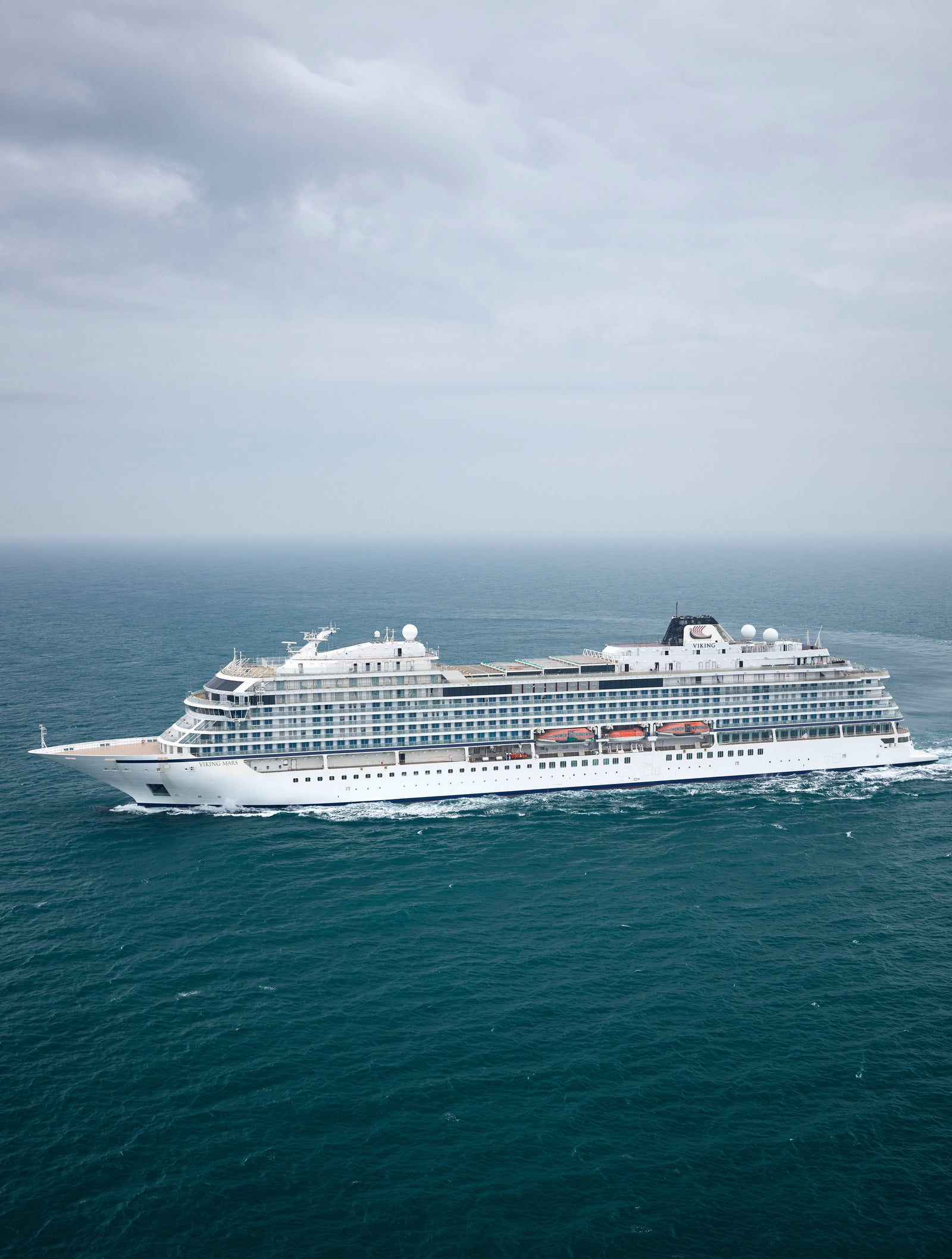 Fincantieri | Group - Business - Products - Cruise Ships - Viking Venus: Large white cruise ship in operation navigating open ocean under cloudy sky, surrounded by calm waters, multiple decks and visible red lifeboats, emphasizing safety and luxury travel.