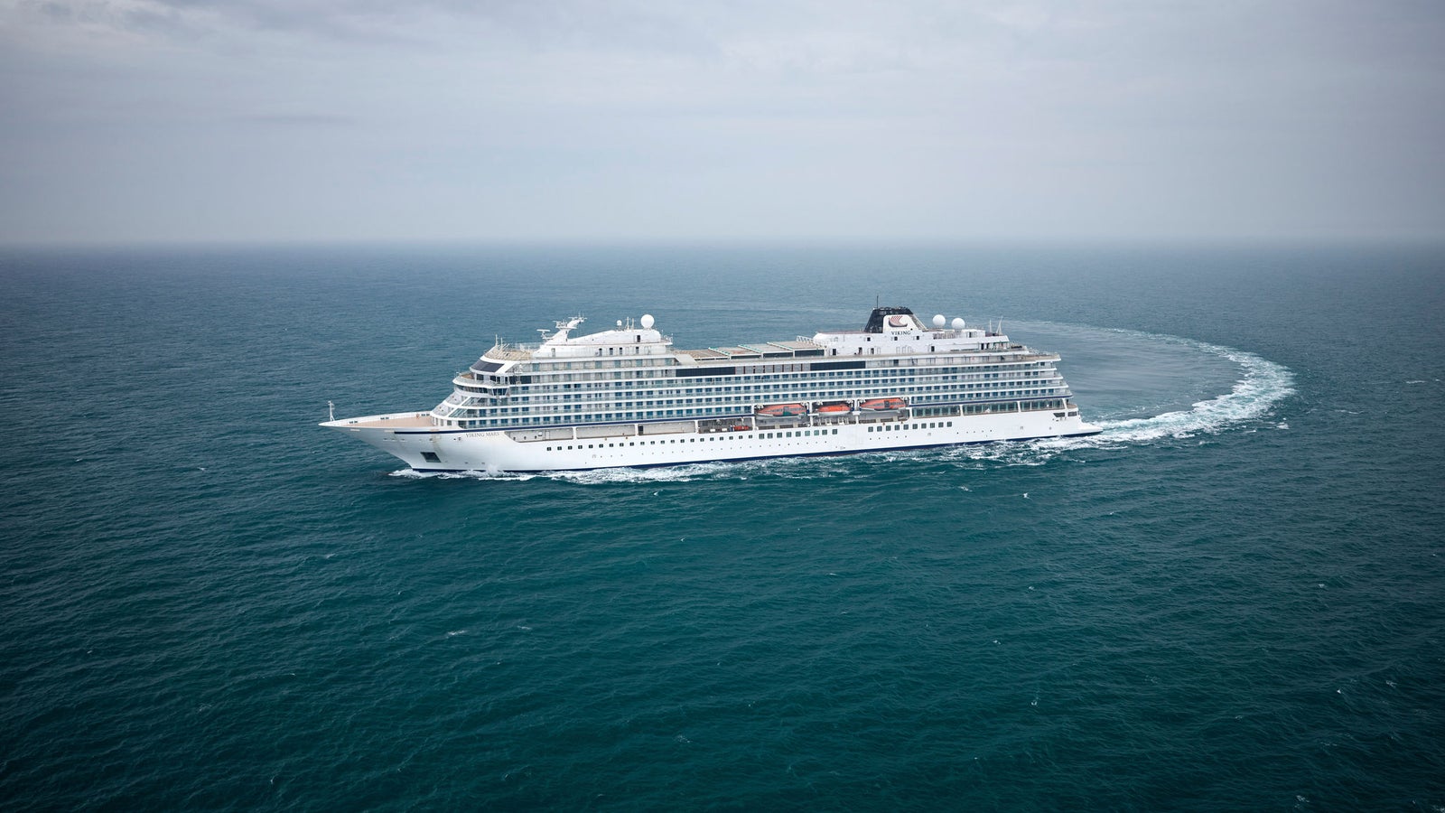 Fincantieri | Group - Business - Products - Cruise Ships - Viking Venus: Large white cruise ship in operation navigating open ocean under cloudy sky, surrounded by calm waters, multiple decks and visible red lifeboats, emphasizing safety and luxury travel.