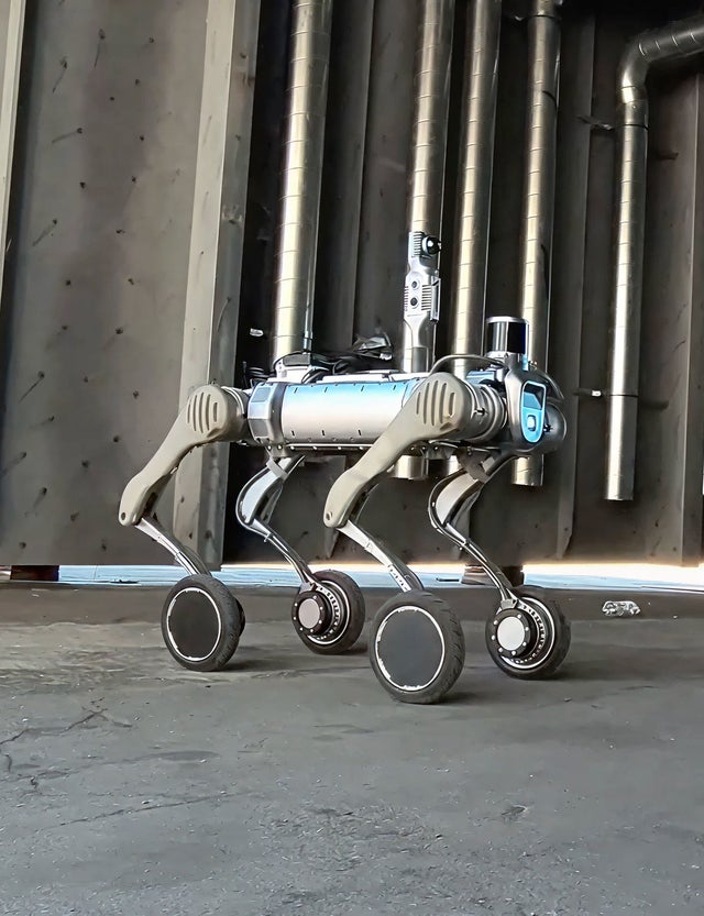 Fincantieri | Group - Sustainability - Responsible Culture - Ethical AI Management: Futuristic four-legged robotic dog with wheels, metallic body equipped with visible sensors and modern design, indoor industrial environment with metal pipes and concrete floor.