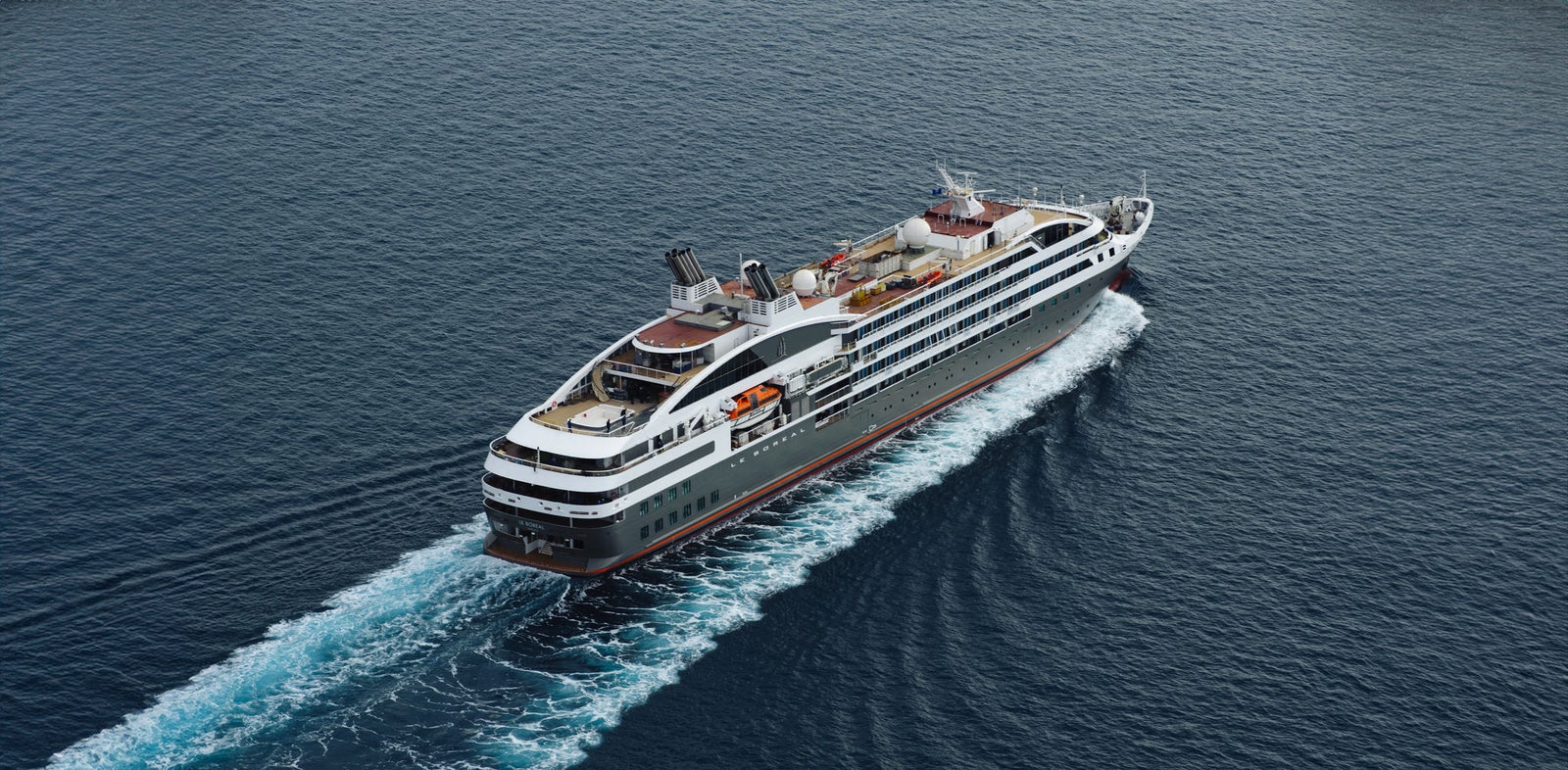 Fincantieri | Group - Business - Products - Cruise Ships - Le Boreal: Modern luxury cruise ship in operation navigating calm deep blue ocean waters, multiple decks, outdoor seating areas, sleek design elements, serene maritime journey with clear skies and gentle waves, no visible text or numeric values on ship.