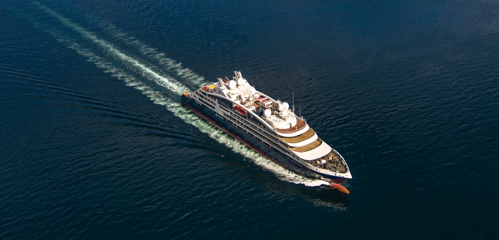 Fincantieri | Gruppo - Business - Prodotti - Navi da Crociera - Le Lapérouse: Vista aerea della nave Le Lapérouse operativa in navigazione su mare aperto, scafo bianco con dettagli color oro, ponti passeggeri multipli, scia visibile in acqua.
