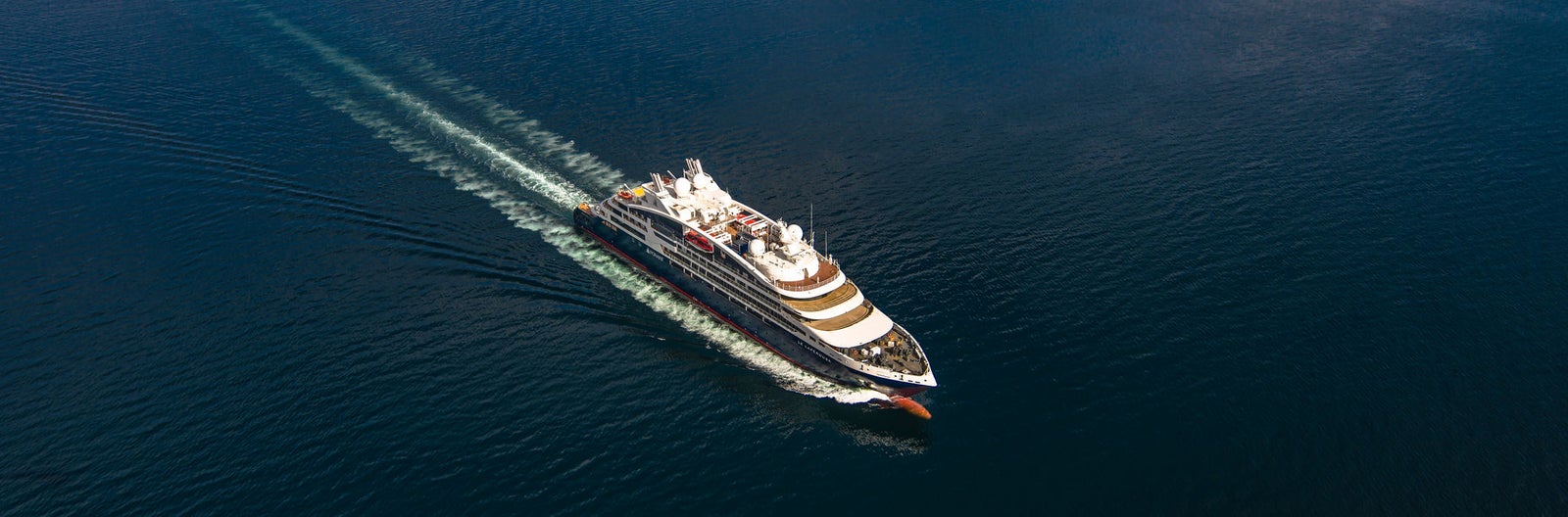 Fincantieri | Gruppo - Business - Prodotti - Navi da Crociera - Le Lapérouse: Vista aerea della nave Le Lapérouse operativa in navigazione su mare aperto, scafo bianco con dettagli color oro, ponti passeggeri multipli, scia visibile in acqua.