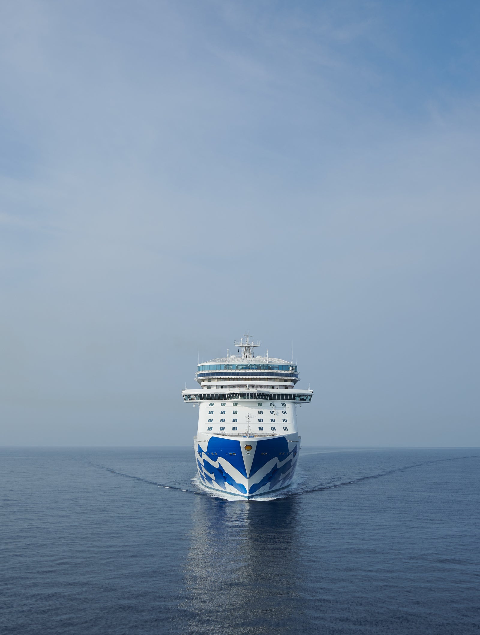 Fincantieri | Gruppo - Business - Prodotti - Navi da Crociera - Sky Princess: Vista di prua della nave Sky Princess operativa in navigazione su acque calme e aperte sotto cielo nuvoloso, design blu e bianco sullo scafo, più ponti visibili.