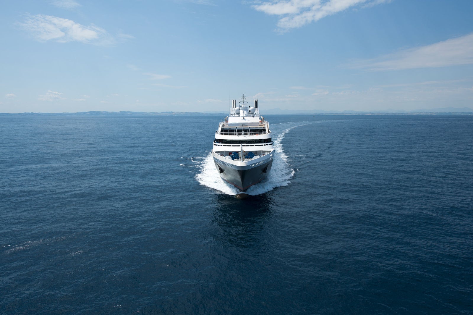  Fincantieri | Group - Business - Products - Cruise Ships - L'Austral: Large modern cruise ship in operation navigating calm open waters under clear blue sky, white with sleek design features, atmosphere of luxury and adventure, ocean stretches endlessly emphasizing tranquility and freedom.