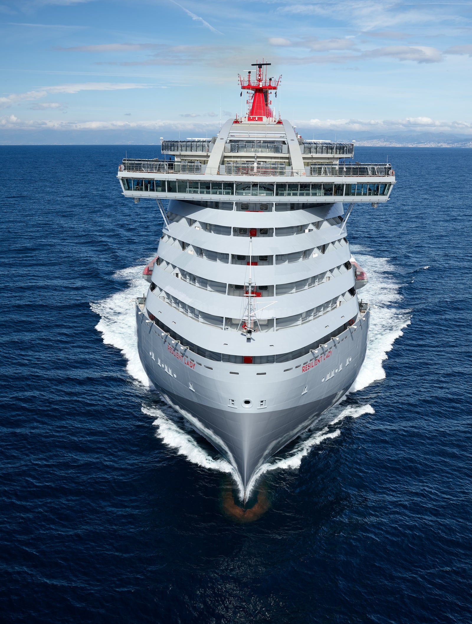 Fincantieri | Group - Business - Products - Cruise Ships - Resilient Lady: Large operational cruise ship with modern design, multiple decks and distinctive red funnel, sailing in calm waters under partly cloudy sky, atmosphere of luxury and adventure.