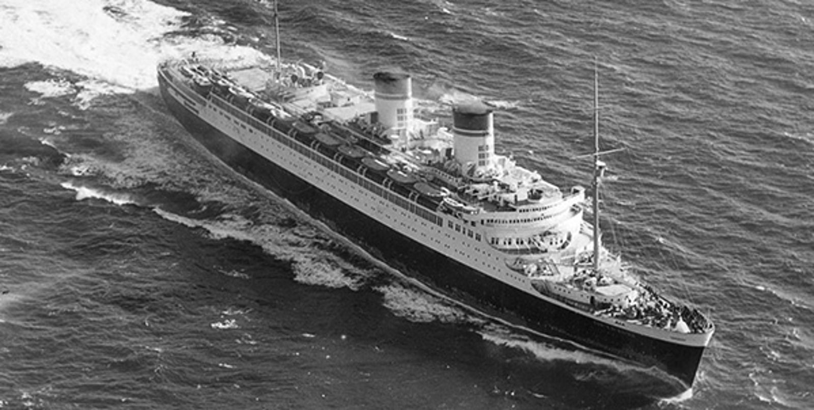 Fincantieri | About Us - Historic Ships: Historic ocean liner 'Victoria' sailing on open waters, impressive design with two funnels and visible flags, name clearly readable on the hull, waves breaking at the bow.