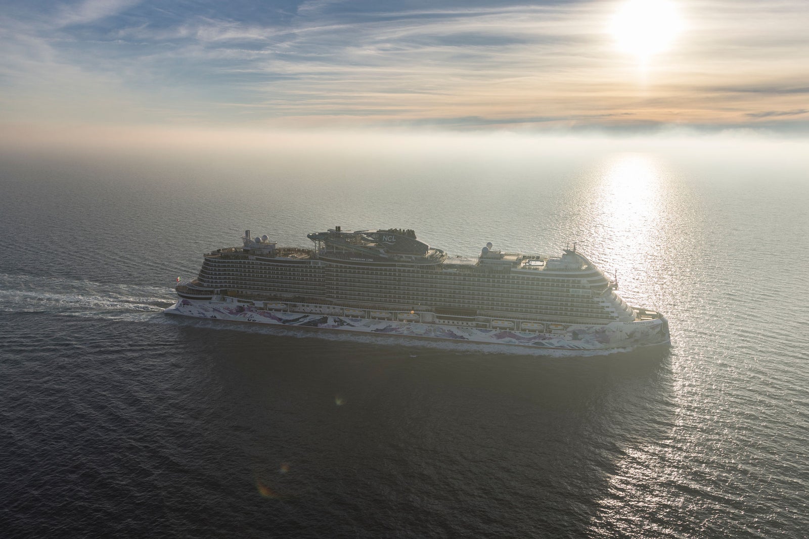  Fincantieri | Gruppo - Business - Prodotti - Navi da Crociera - Norwegian Luna: Vista completa del lato di dritta della nave da crociera Norwegian Aqua con livrea colorata sullo scafo, cielo blu e mare calmo.