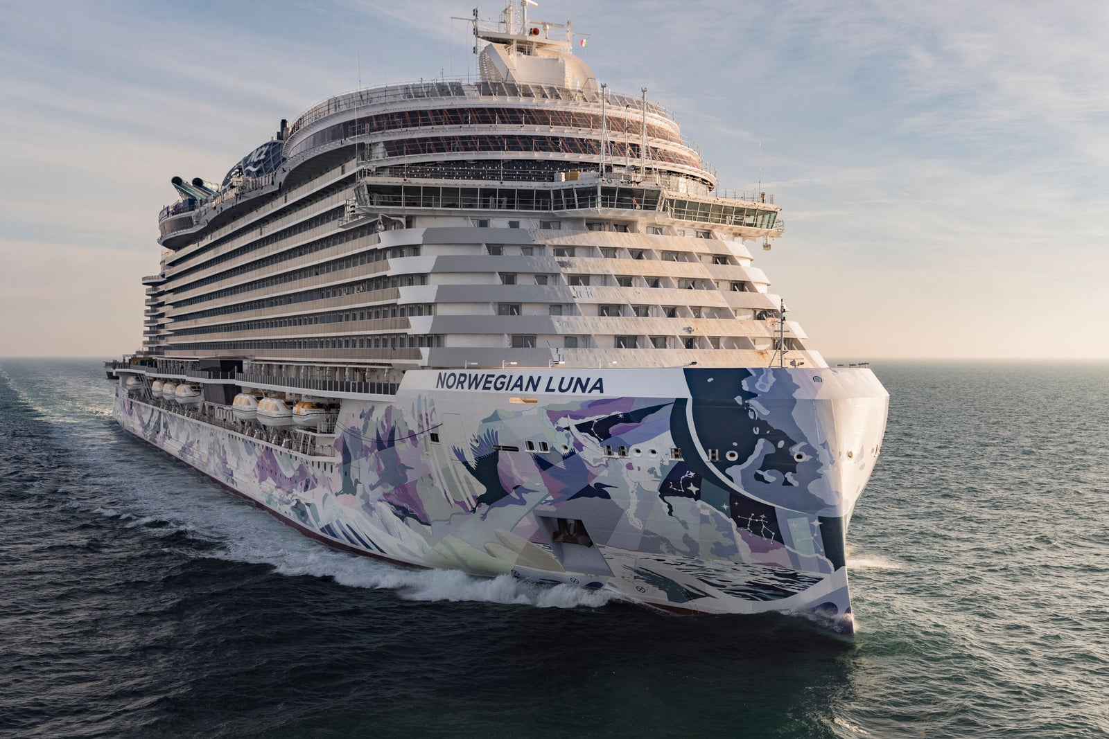 Fincantieri | Gruppo - Business - Prodotti - Navi da Crociera - Norwegian Luna: Grande nave da crociera operativa con vibrante e colorata opera d’arte sullo scafo, vista laterale, in navigazione al tramonto.