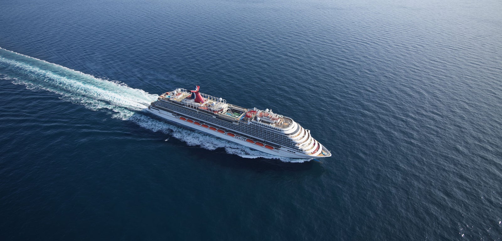 Fincantieri | Gruppo - Business - Prodotti - Navi da Crociera - Carnival Panorama: Grande nave da crociera operativa naviga su oceano aperto sotto cielo blu limpido, più ponti e accenti rossi e bianchi vivaci, acqua calma crea scenario sereno ed espansivo, enfatizzando viaggio e grandezza.