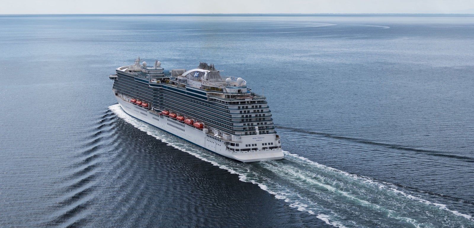 Fincantieri | Group - Business - Products - Cruise Ships - Regal Princess: Stern view of large operational white cruise ship sailing on calm open waters under partly cloudy sky, bow clearly visible with elegant and majestic design.