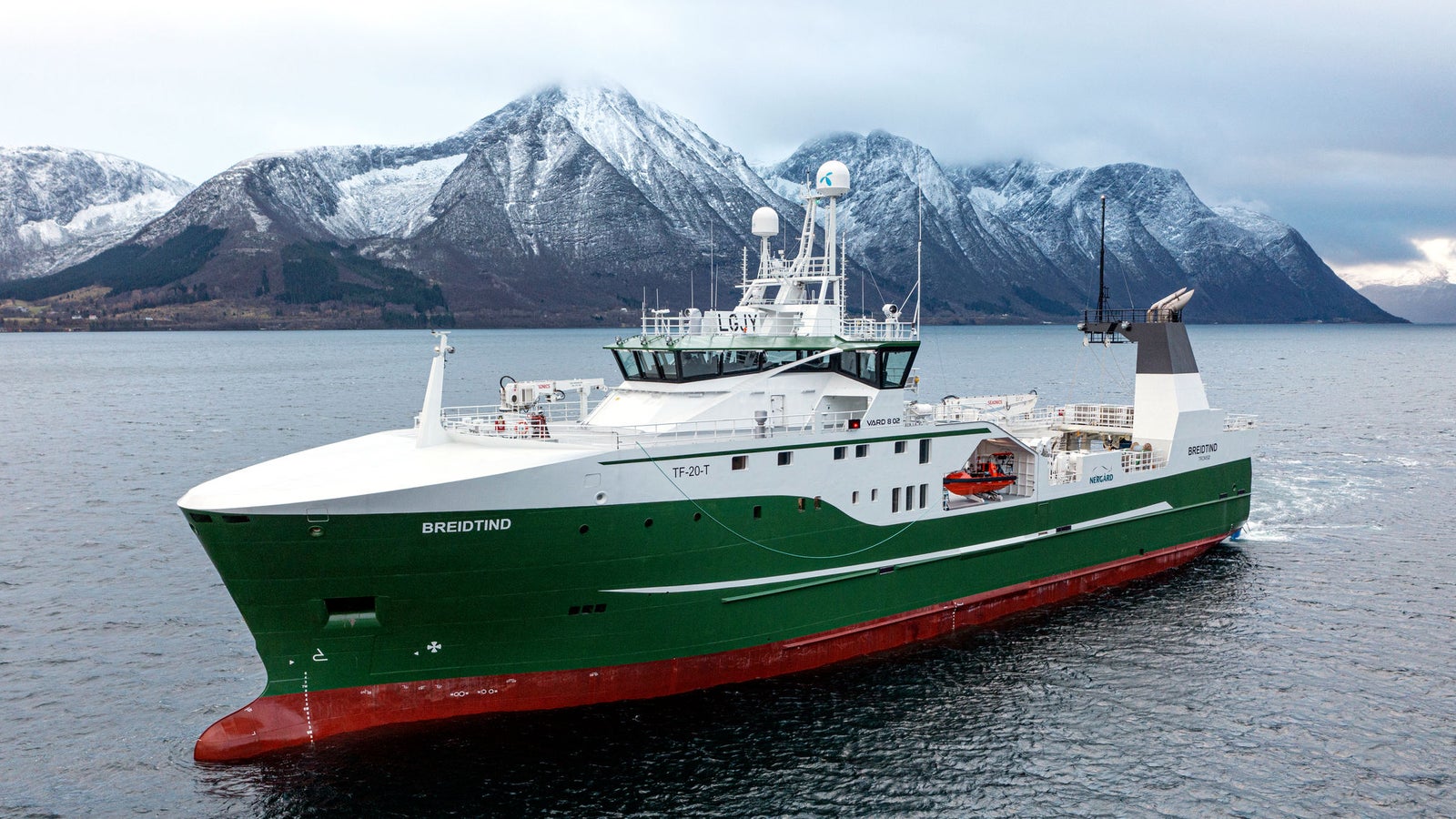 Prodotto - Peschereccio Brødrene: Vista laterale della nave operativa in navigazione, scafo verde e bianco con nome Brødrene visibile, attrezzature moderne, sfondo con montagne innevate, ambiente marittimo freddo.