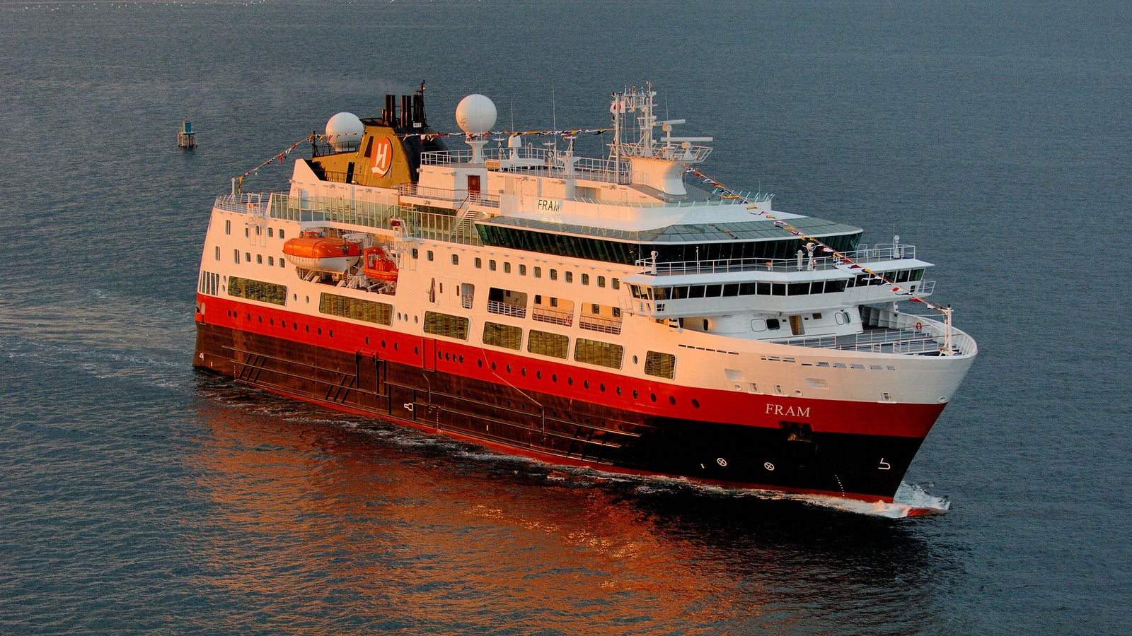 Fincantieri | Group - Business - Products - Cruise Ships - Fram: Imposing operational ship with red and white livery, visible lifeboats and communication domes, 'Fram' name clearly visible on hull, sailing on calm waters at sunset, warm lighting highlights architectural details, atmosphere of maritime serenity and elegance.