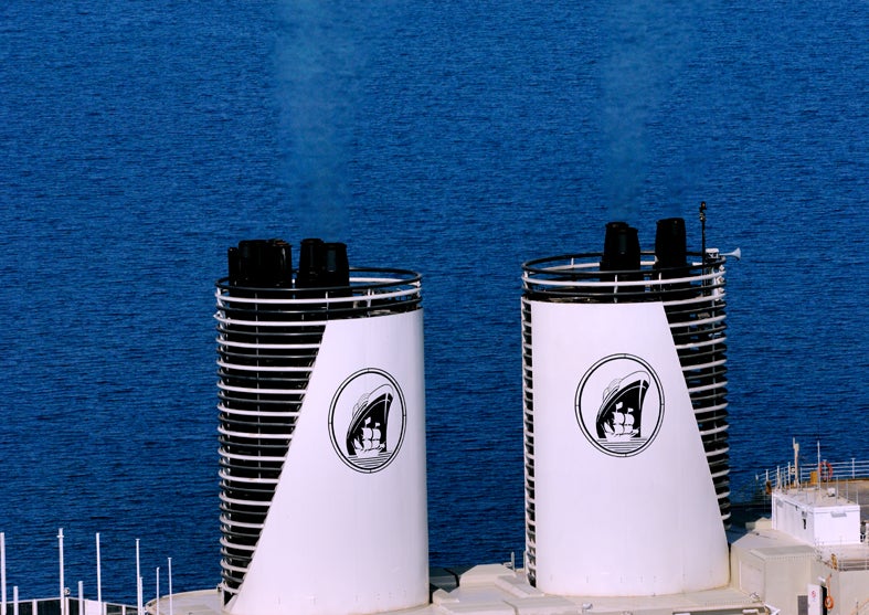  Fincantieri | Gruppo - Business - Prodotti - Navi da Crociera - Eurodam: Due grandi fumaioli bianchi con cima nera e logo con nave a vela in design circolare, su nave da crociera operativa, sfondo di oceano aperto con acque calme e blu fino all’orizzonte.