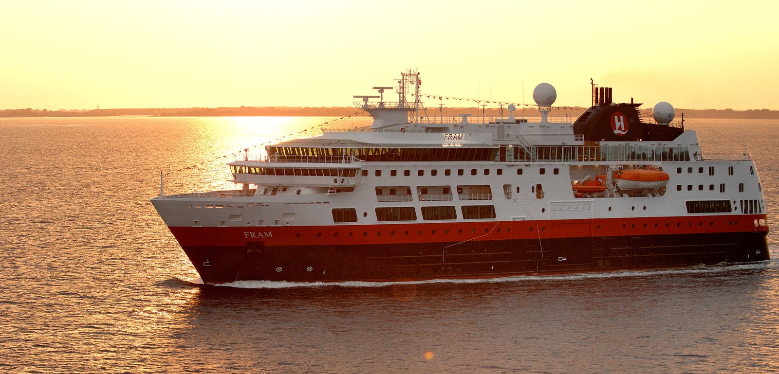 Fincantieri | Group - Business - Products - Cruise Ships - Fram: Large operational cruise ship with red and white exterior, visible lifeboats and antennas, 'Fram' name clearly readable on hull, sailing on calm waters during golden sunset, warm lights highlight details and create a serene and refined atmosphere