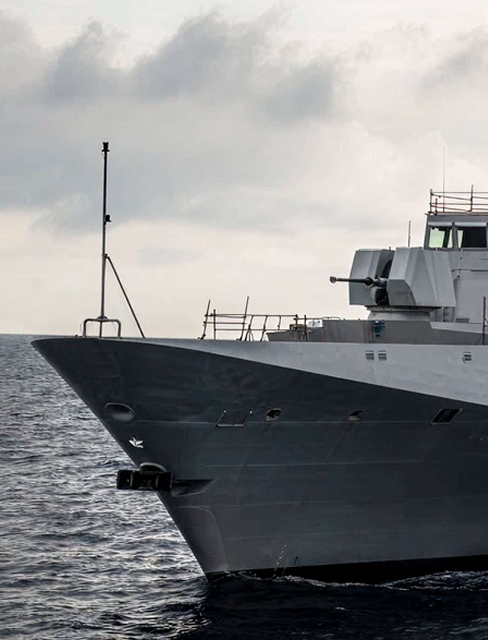 Fincantieri | Group - Companies - Subsidiaries and Affiliates - Fincantieri Arabia: Modern naval ship operationally sailing on calm waters under a cloudy sky, angular design details and advanced radars, emphasis on maritime technology.