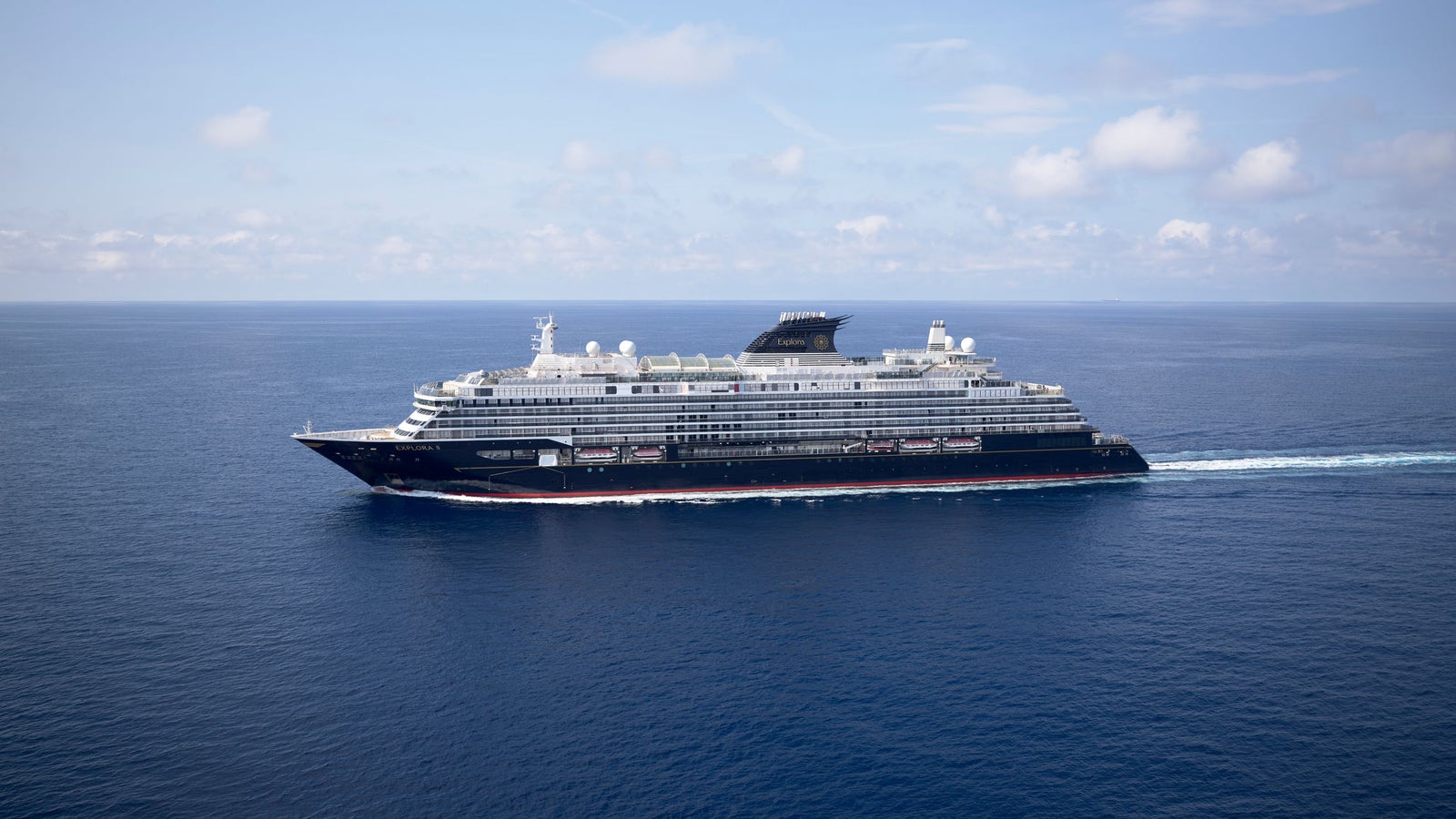Fincantieri | Group - Business - Products - Cruise Ships - EXPLORA II: Side view of operational cruise ship in navigation, sleek black and white design, multiple decks and visible amenities, name Explora X clearly visible on hull.