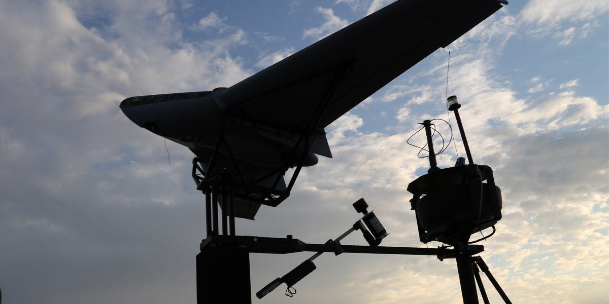 Fincantieri | Group - Business - Products - Telecommunications - Drone launch system: Drone mounted on launch system against cloudy sky, several antennas and sensors visible on apparatus.