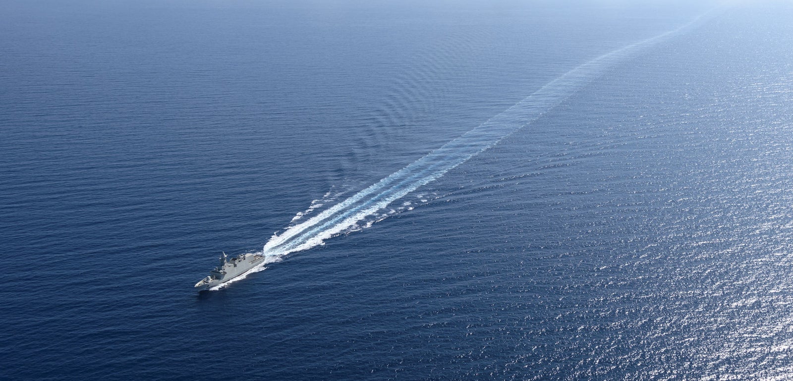 Fincantieri | Group - Business - Products - Defence Vessels - Corvettes - Abu Dhabi class: Aerial view of operational ship underway, prominent wake, crossing calm open waters.